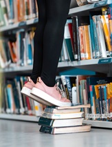 Someone standing on a stack of books, in front of a book shelf.