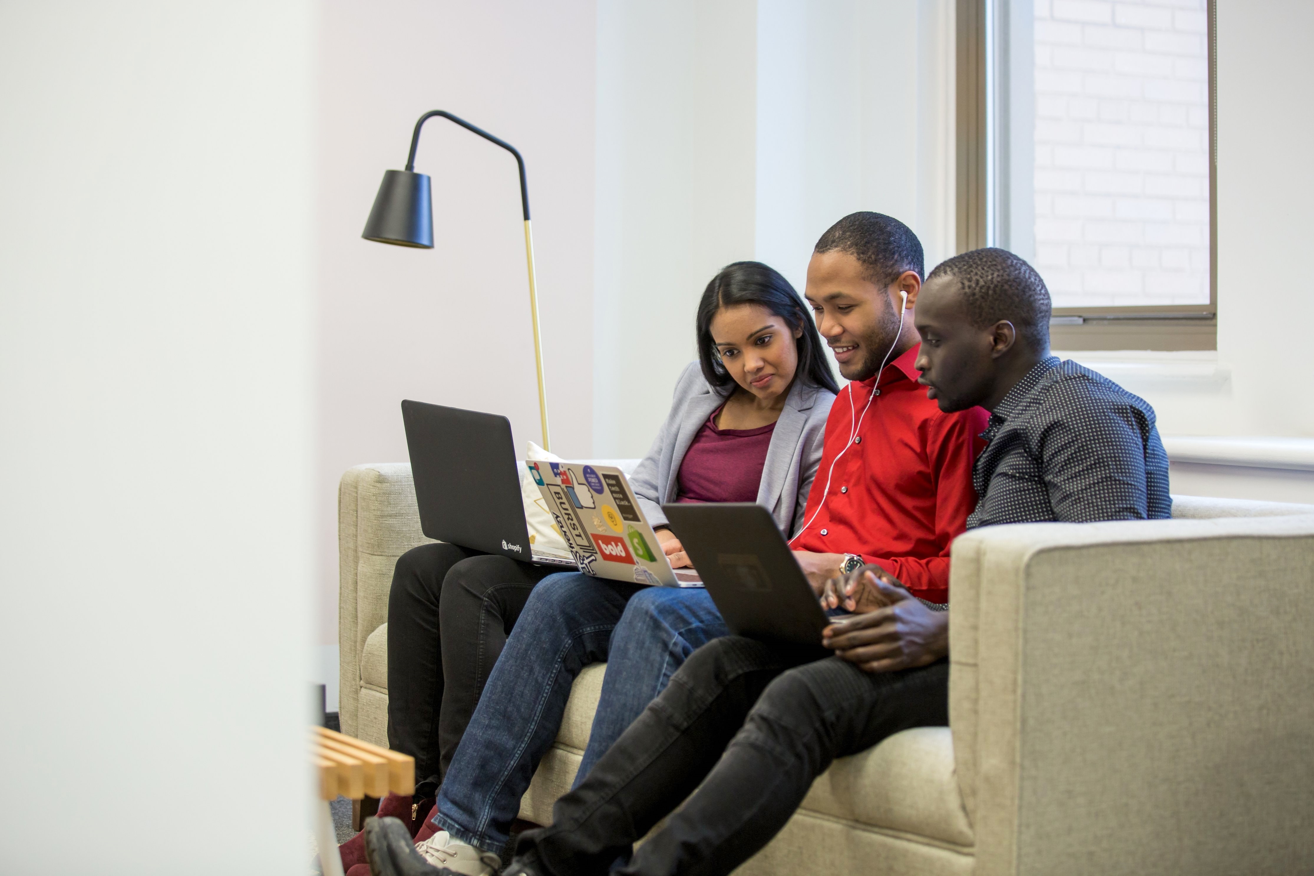 3 adults on a couch with open laptops