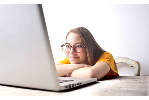 photo of a young woman wearing glasses with long hair smiling at her laptop screen