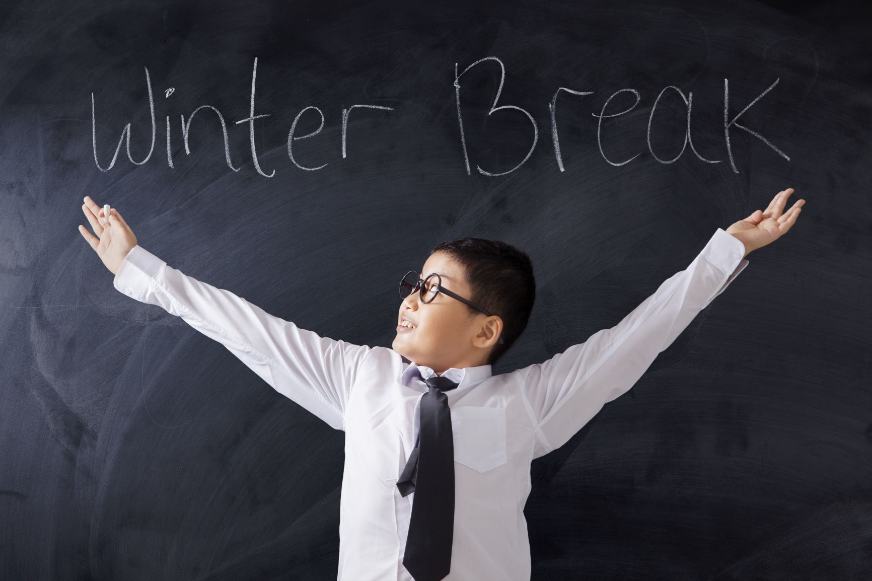 schoolage child with outspread hands in front of a chalkboard that says winter break