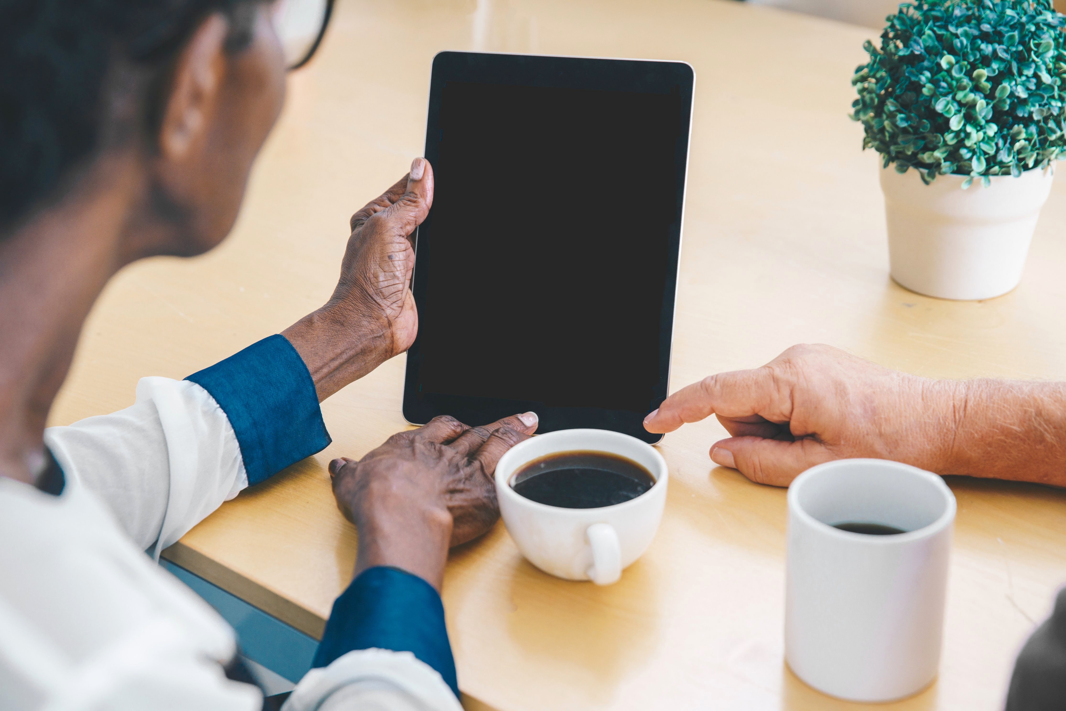 Two people looking at a tablet with coffee cups nearby
