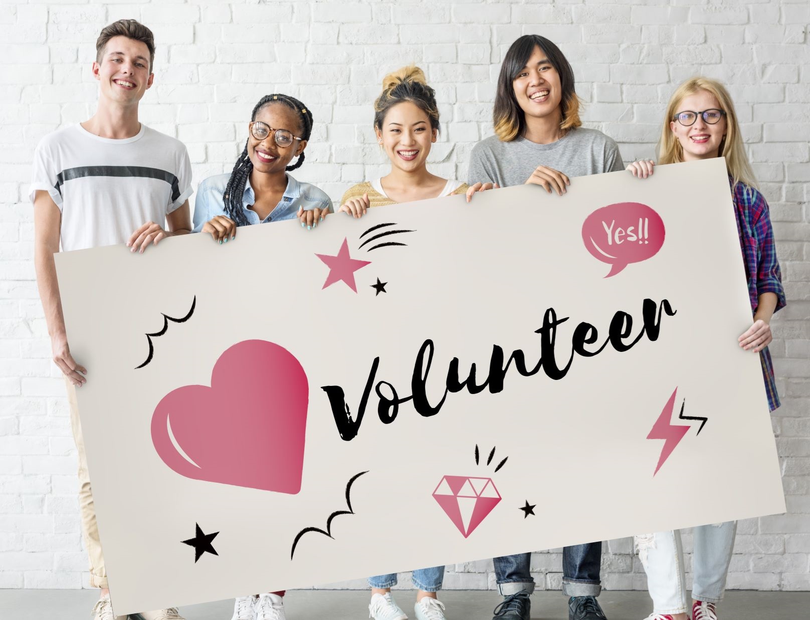 five smiling teens holding a sign that says volunteer on it. 