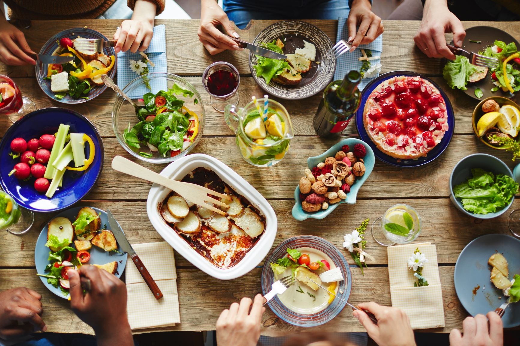photo of a table filled with food and hands poised to eat