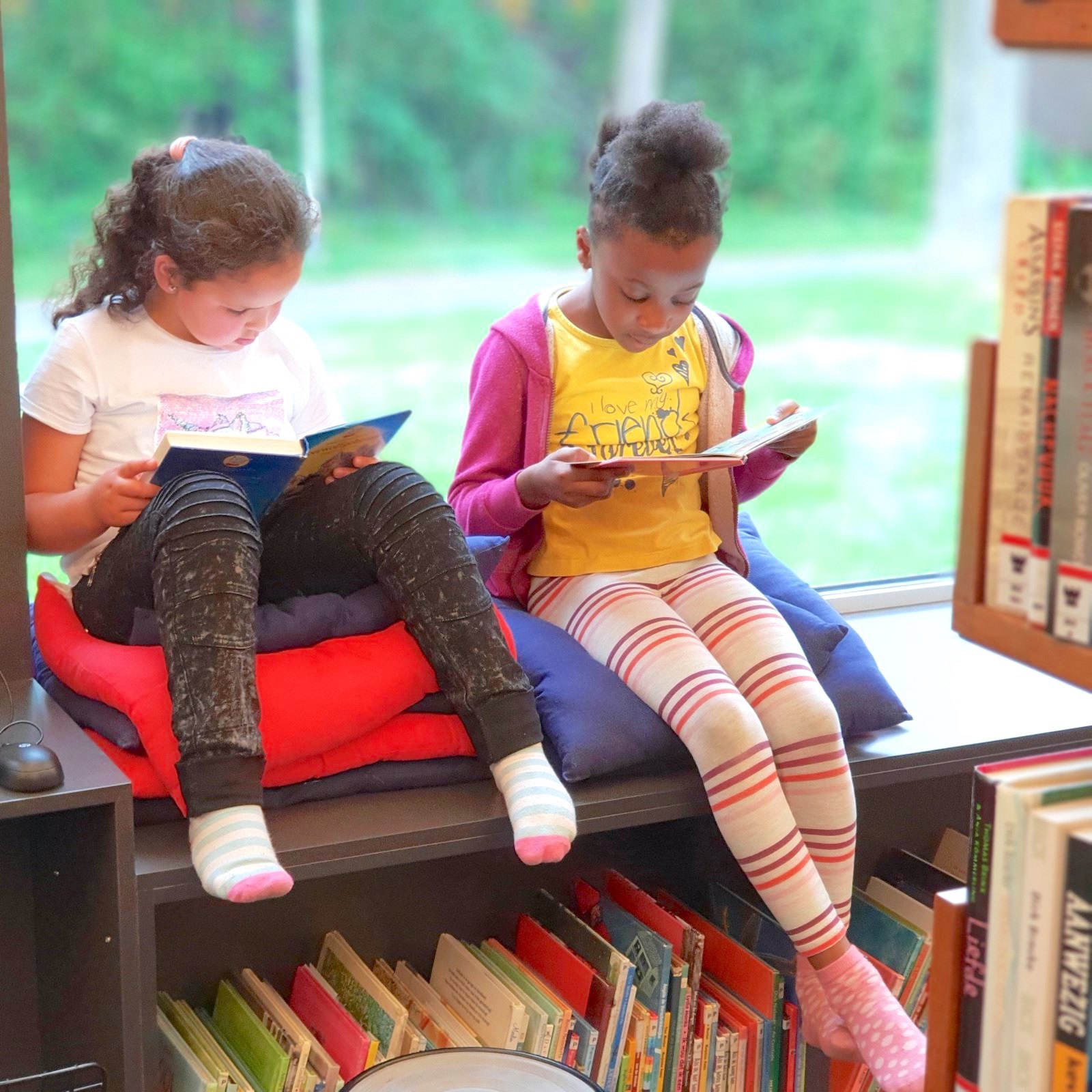 two school age girls reading books in front of a window