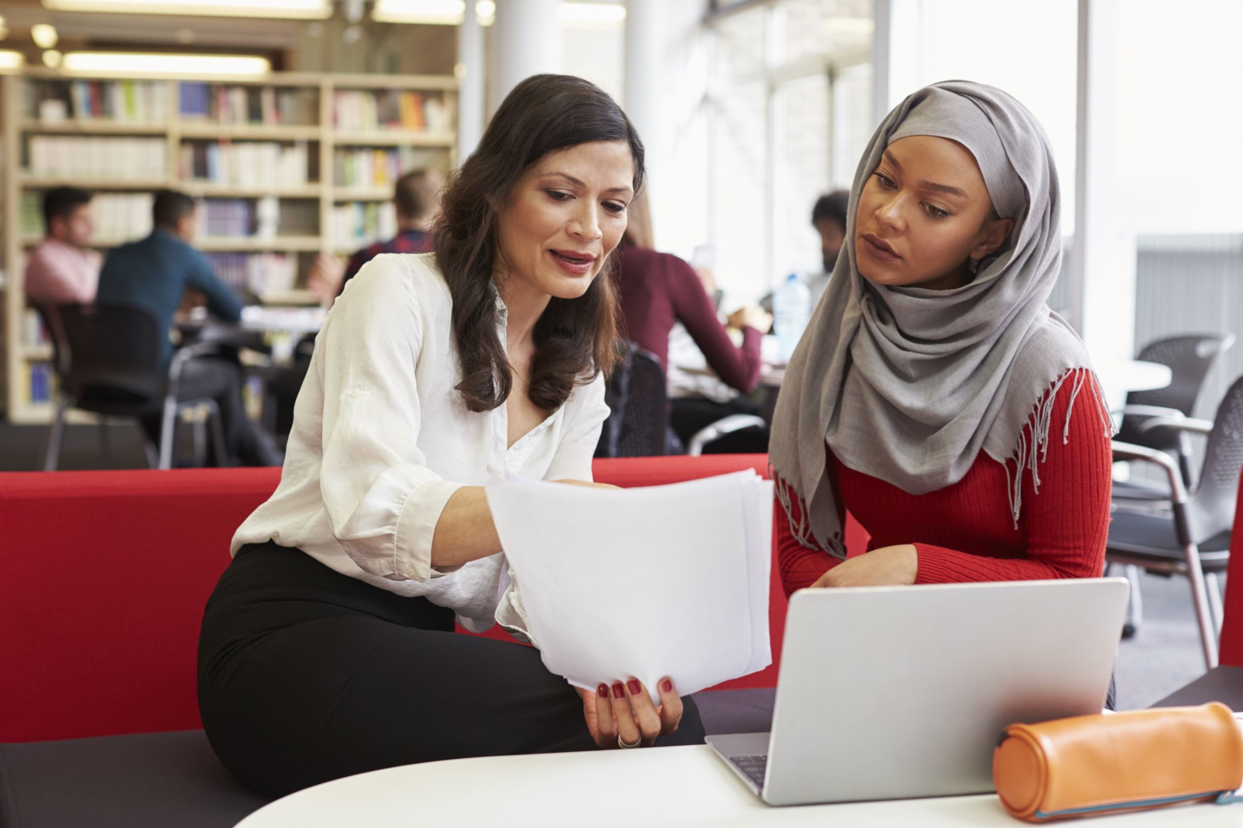 Two women holding a document, one appears to be explaining the content to the other.