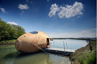 This wooden, egg-shaped home floats on the water, moored to a dock.