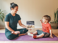 A child and an adult holding a picture book sit together on a yoga mat.