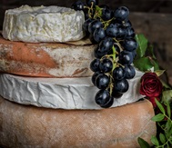 A bunch of grapes lies draped over a stack of wheels of cheese.