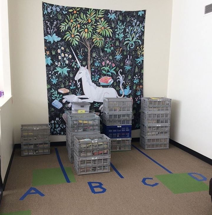 "The Unicorn is Reading" wall hanging by Steph Terao watches over organized crates full of library materials.