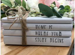 A decorative book stack with the words "Home is where your story begins"