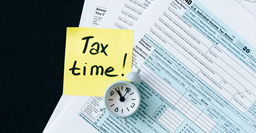 Tax forms with a small clock and yellow note on top that reads "Tax time!"