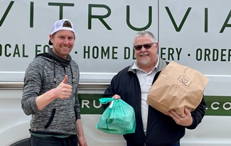Picture of Vitruvian Farms co-owner Tommy Stauffer with gift card winner David Wilcke in front of the Vitruvian Farms delivery vehicle. Tommy is giving a thumbs up gesture and David is holding bags of products he purchased with his gift card.