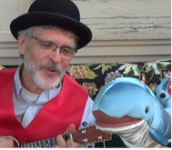 Picture of Milwaukee Steve wearing a red vest and black hat singing with a whale stuffed animal.