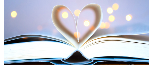 Closeup picture of open book against a light purple background with soft lights. The middle pages are folded to form a heart shape.