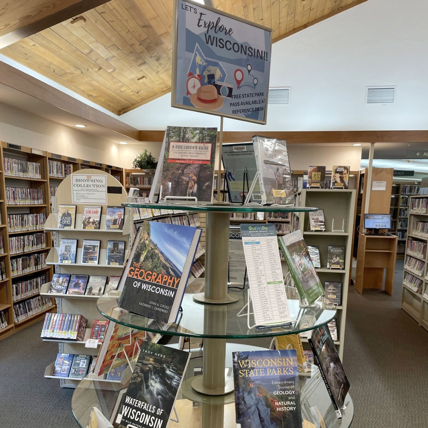A display shelf with glass tiers of books, DVD's and information cards about Wisconsin recreation inside Elm Grove Public Library.