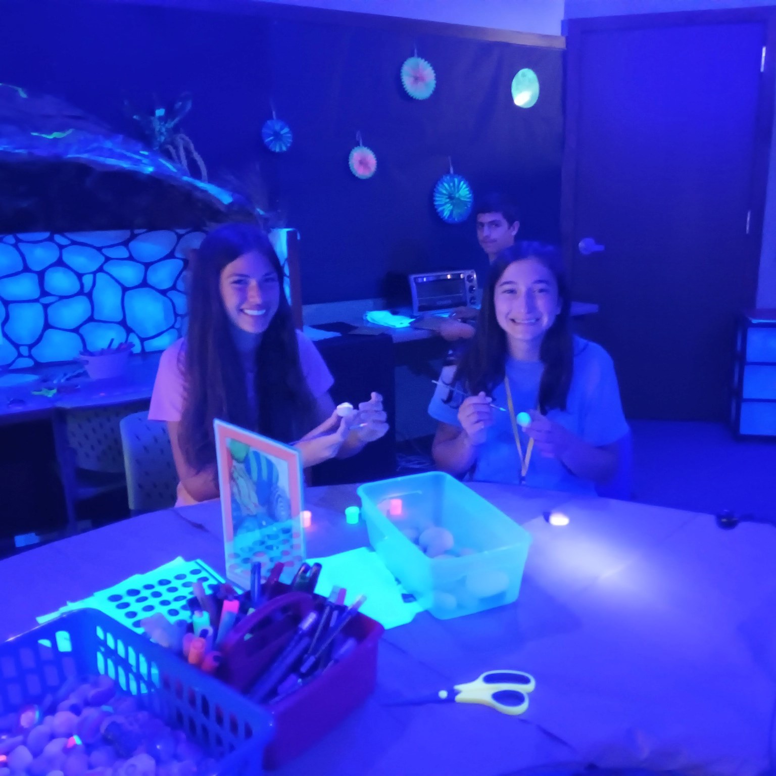 Three children in a low-lite room with glow-in-dark artwork on the walls around them.
