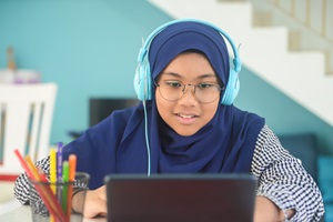 Teen with headphones on while looking at computer and writing a book review