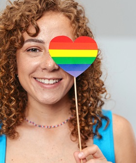 Woman holding up rainbow coloured heart on a stick