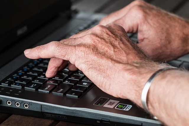 A photograph of an older person typing on a laptop.