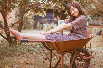Asian-American teen girl sitting happily in wheelbarrow in a garden