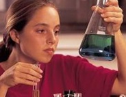 Red-headed girl holding and looking at a beaker of blue liquid.