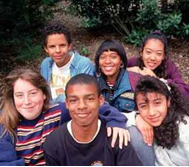 Diverse group of teens sitting on the ground smiling at the camera.