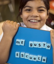 Smiling girl holds board that reads I like school in Spanish