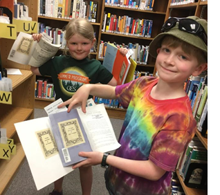 Photo of Cora and Zach holding books they donated, pointing to bookplates with their names