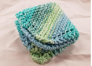 Photograph of a knit washcloth in multicolored blue and green yarn, folded