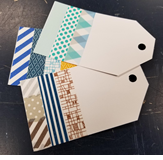 A photo of three gift tags cut from white cardstock and decorated with colorful washi tape