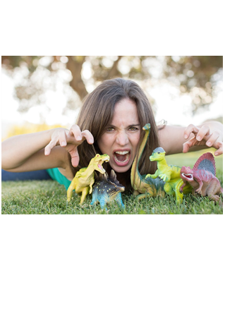 Photograph of summer reading performer Nathalia laying on green grass outside, making a fierce face, with plastic dinosaur toys in the foreground