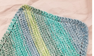 Photograph of a knit washcloth laid flat in multicolored blue and green yarn