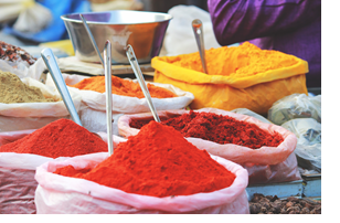 Photo of red and orange spices mounded in fabric bags with silver spoons in them