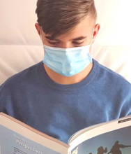 A person wearing a mask reads a book.