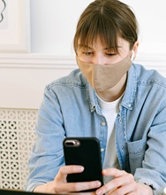 A person wearing a mask looks at a smartphone.