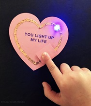 Completed circuit card with glowing LED and text reading "You light up my life".