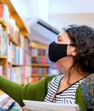 A person wearing a mask browses a bookshelf.