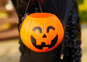 A trick-or-treater holds a jack-o-lantern shaped candy basket.