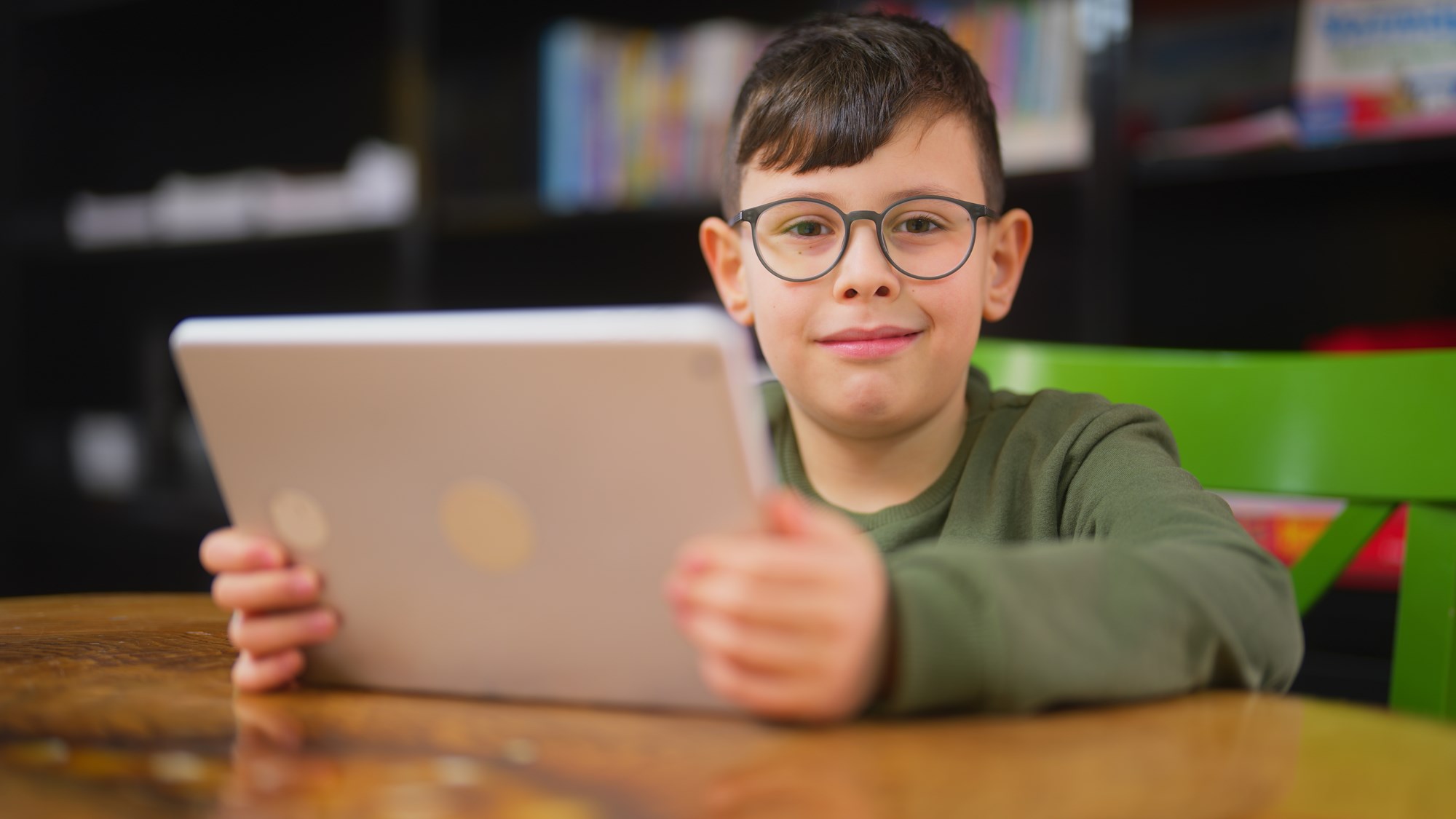 Child with Glasses Holding a Tablet and Looking Forward