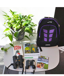 Picture of a table with a plant, backpack, birding books and binoculars.