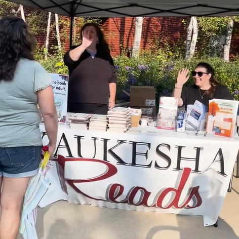 Photo of the Waukesha Read booth at Apple Harvest Festival with library staff waving.