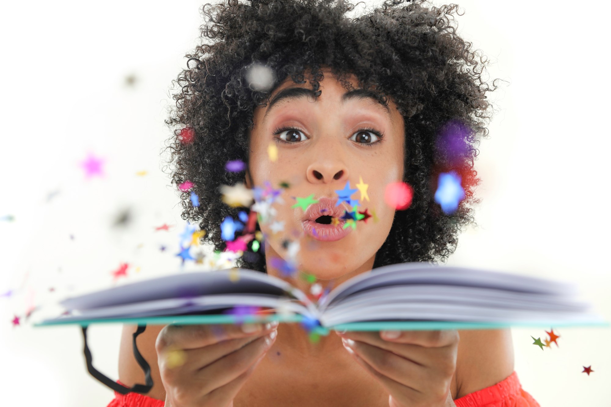 Photo of a woman holding an open book and blowing colorful star confetti out of it.