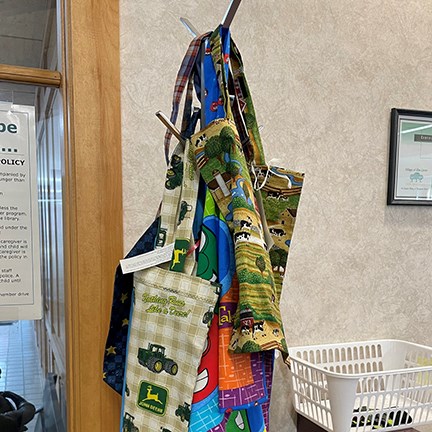 Photo of several handmade cloth bags in different fabrics hanging on a coat rack in the library.