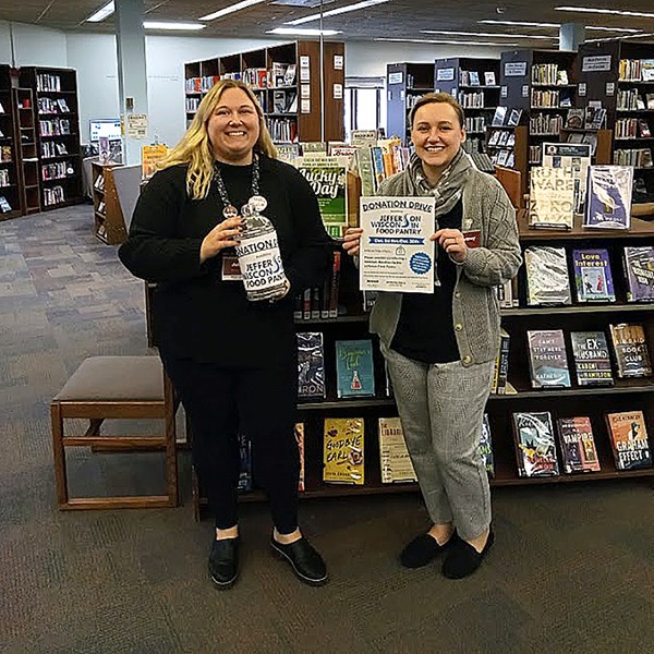 Photo of two Jefferson Public Library Staff holding up the Donation Drive information inside the library in front of shelves.