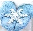Close-up photo of someone's hands wearing light blue mittens and holding a large model of a white snowflake.
