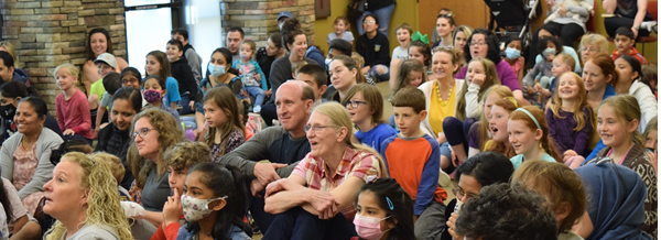 A mixed-age crowd of people with happy and surprised faces as they watch a magic show at the Post Road Library.
