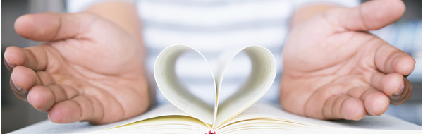 hands around pages of a book curled inward to make a heart shape.