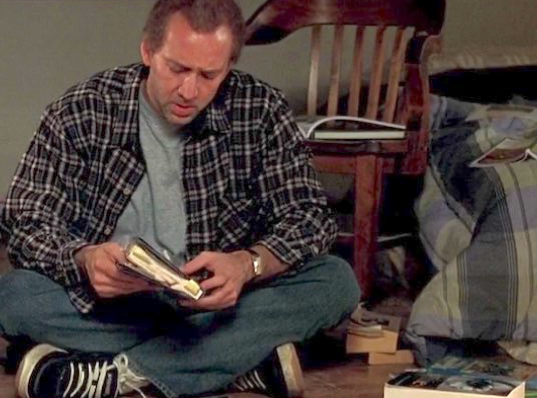 A screenshot from the movie Adaptation, showing a man sitting on the floor and looking at a book.