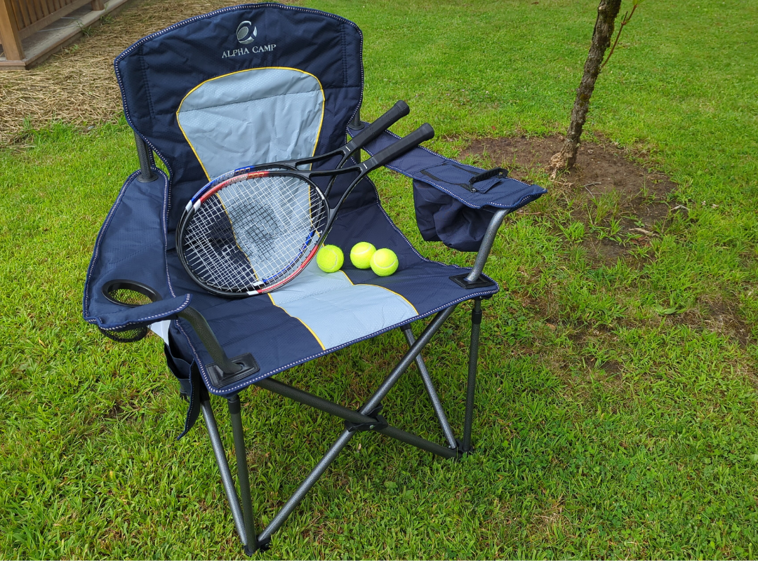 A photograph of a two tennis rackets and three tennis balls artfully arranged on the seat of a folding camping chair.