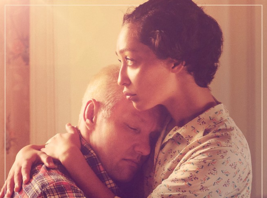 The movie poster for "Loving", depicting a woman holding a man close to her chest, with golden light.